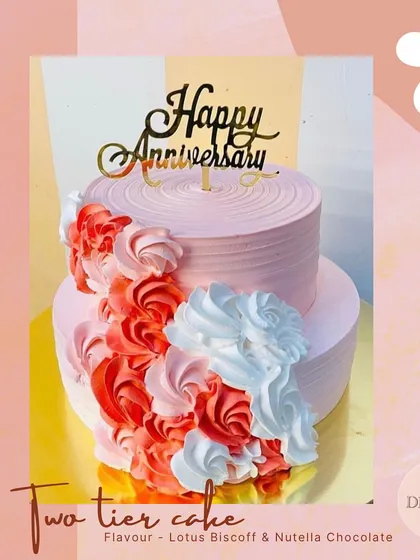 A beautiful two-tier anniversary cake featuring a cascade of red, pink, and white frosting rosettes. This design offers a vibrant and textured look, with Lotus Biscoff and Nutella Chocolate flavors inside.