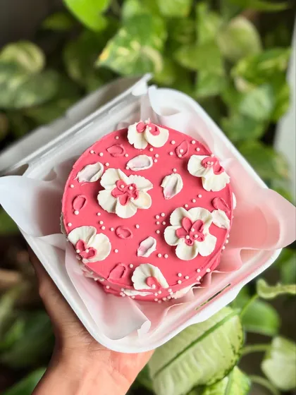 A hand-held shot of the floral bento cake, showing its cute size and vibrant pink color against a leafy background.