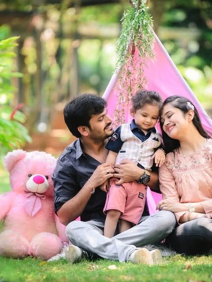 This family portrait captures a loving moment between parents and their child in a pink tent setup outdoors. The soft smiles and gentle interaction make this a beautiful memory.