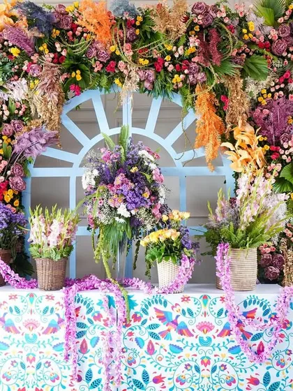 A stunning floral wall designed for a Haldi ceremony entrance. This explosion of colorful flowers in shades of purple, orange, yellow, and white creates a breathtaking welcome for guests and a perfect photo opportunity.