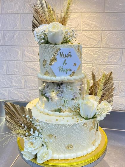 This three-tier wedding cake for Krish and Kripa features intricate stencil work, gold leaf, and beautiful dried botanicals. The middle tier is a clear separator filled with lights and flowers for a modern touch.