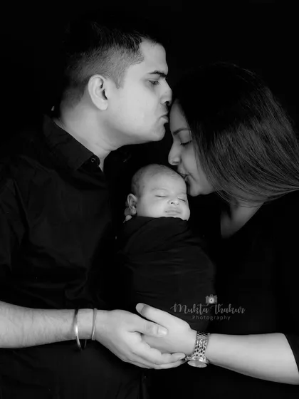 A black and white portrait showing the new parents' love for their baby, with gentle kisses and a protective embrace.