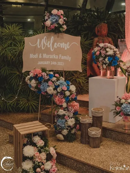 A rustic yet chic welcome sign. The simple wooden board is elevated by a cascade of beautiful pink, blue, and white flowers, creating a stunning welcome piece.