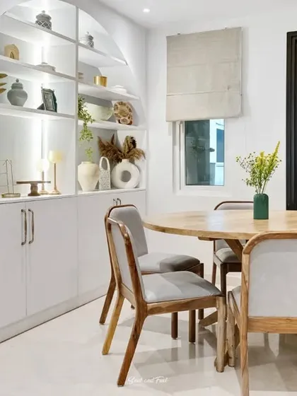 An elegant dining area with a round wooden table and an arched, built-in display cabinet. The clean lines and neutral colors create a modern yet timeless space for meals.