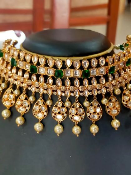 The choker necklace worn by the client. This piece features two layers of Kundan with green stones and pearl drops, making it a versatile choice for various events.