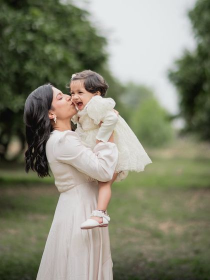 A mother kissing her laughing daughter on the cheek during an outdoor session.