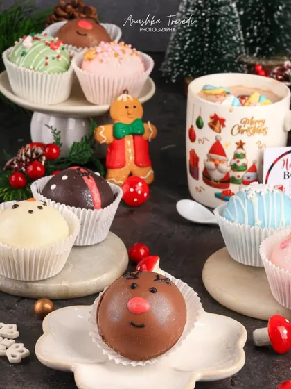 An assortment of Christmas-themed hot cocoa bombs, including a cute reindeer one. The styling is playful and highlights the fun, interactive nature of the product.