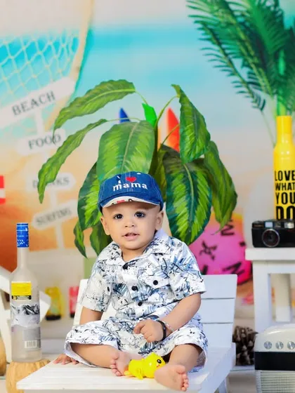 This little beachgoer, wearing a "Mama" cap, is ready for some fun in the sun. The colorful backdrop makes for a lively and cheerful portrait.