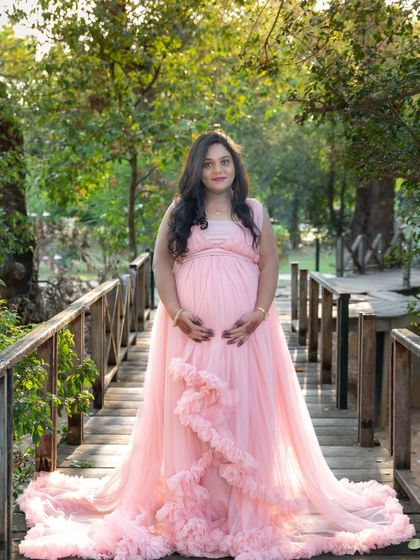 A beautiful portrait of a mom-to-be on a wooden bridge in a park, wearing a lovely pink ruffled gown.
