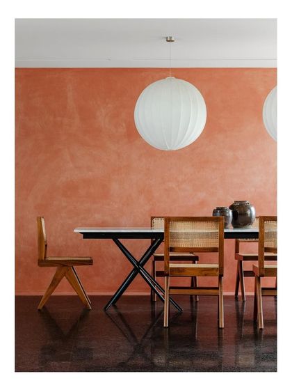 The dining table, with its clean white top and black X-frame base, stands out against the textured terracotta wall. I design furniture to create a dialogue with the architecture of a space.
