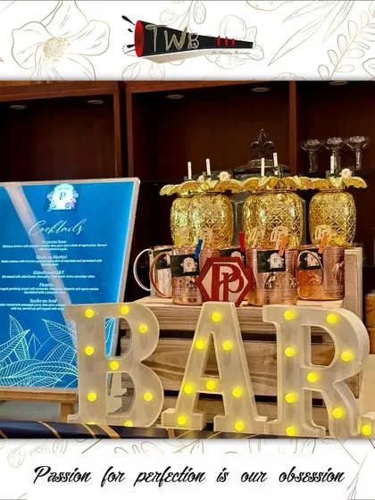 A modern and chic bar setup featuring an illuminated "BAR" sign, pineapple-shaped mugs, and a sleek, backlit menu for an engagement party at Aurika, Mumbai.