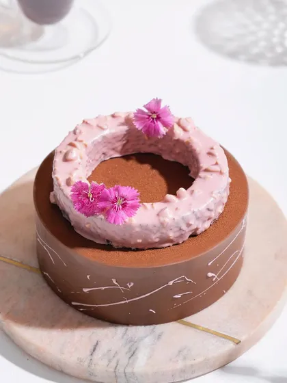 A close-up of the Belgian Chocolate and Raspberry Entremet, focusing on the textured raspberry ring and delicate flower garnish.