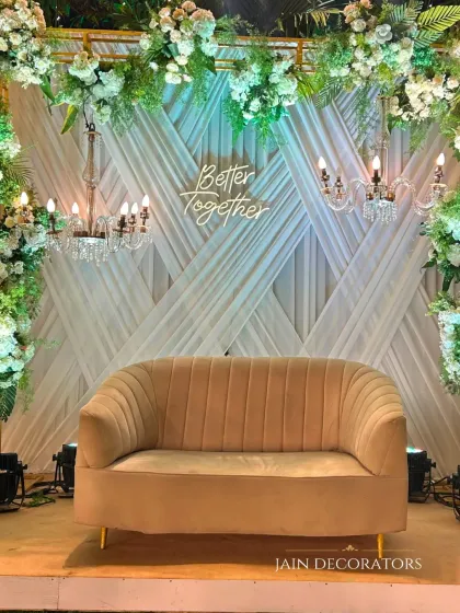 A cozy and chic stage for a more intimate gathering. The "Better Together" neon sign adds a personal touch, while the backdrop of white drapes, chandeliers, and greenery creates a romantic and stylish setting.