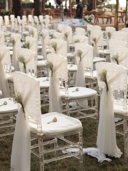 We pay attention to every detail, including the guest seating. Here, clear acrylic chairs are elegantly draped with white fabric and a sprig of baby's breath.