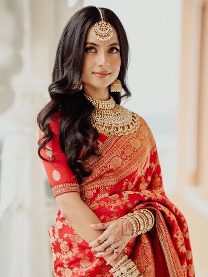 A classic South Indian bride in a red and gold silk saree. Her makeup is timeless and elegant, with defined eyes and a soft glow, perfectly complementing her traditional jewelry.