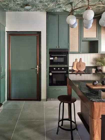 This view of the green kitchen highlights the built-in appliance tower and the patterned wallpaper on the ceiling, which adds an unexpected layer of detail and personality to the space.