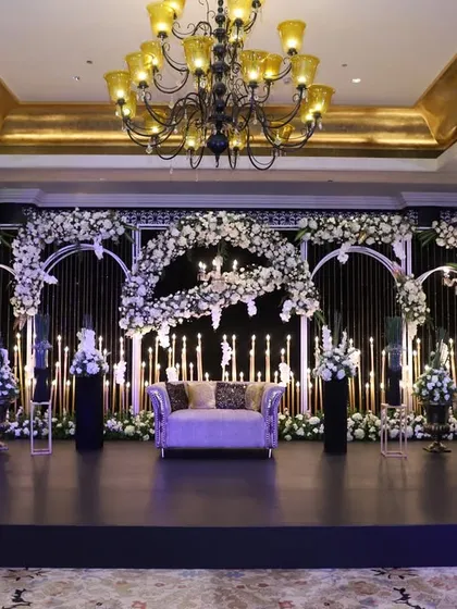 A dramatic and romantic reception stage, featuring a backdrop of black drapes and arches, lit by a sea of candles and adorned with cascading white florals.