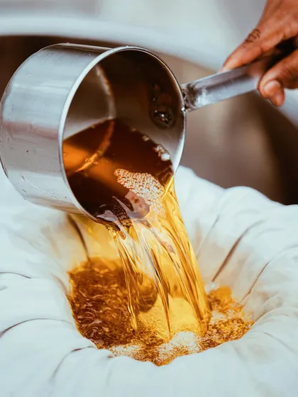 An action shot of fresh, golden ghee being poured and filtered. This image highlights the traditional process and the pure, high-quality nature of the product.