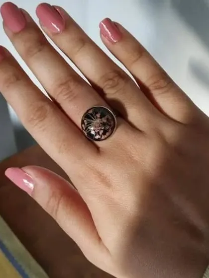 This simple ethnic ring features a delicate pink flower preserved under a clear resin dome. It's a lovely, understated piece that adds a touch of floral charm.