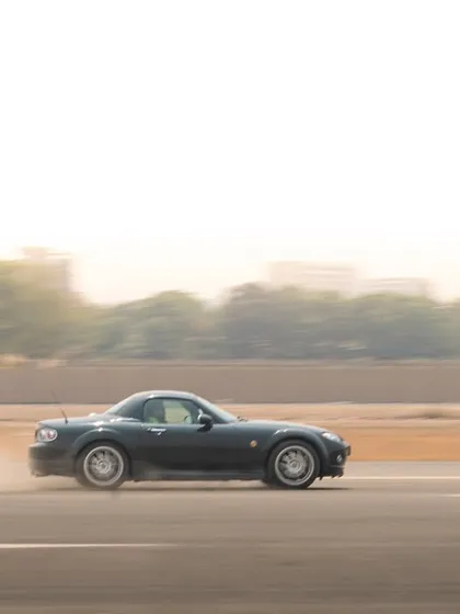 A classic rolling shot of a black Mazda Miata, demonstrating the technique of matching the car's speed to create a crisp subject against a blurred background.