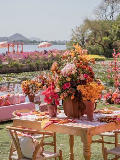 A dining table with a stunning centerpiece of orange and pink flowers, set against the beautiful lily pond of The Oberoi Udaivilas.