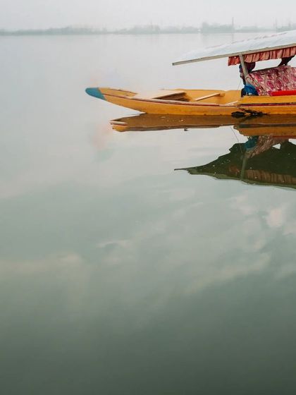 An atmospheric shot of a lone Shikara boat on the misty waters of Dal Lake, setting the scene for a romantic Kashmir story.
