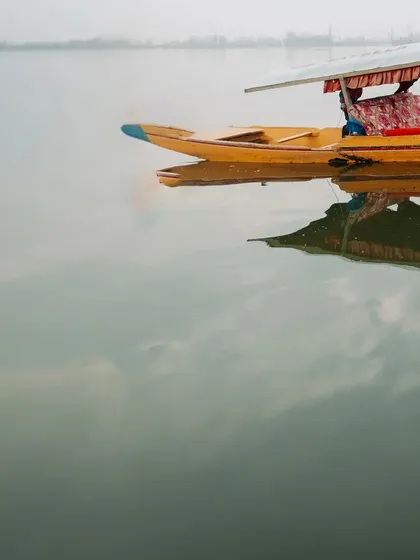 An atmospheric shot of a lone Shikara boat on the misty waters of Dal Lake, setting the scene for a romantic Kashmir story.