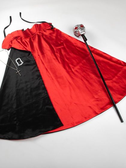 A flat lay of a Dracula costume, including the red and black cape, cross necklace, and skull staff.