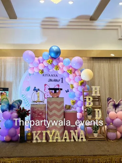 A full view of the stage for the butterfly-themed first birthday party. The setup includes a custom backdrop, themed pedestals, and a photo milestone board.