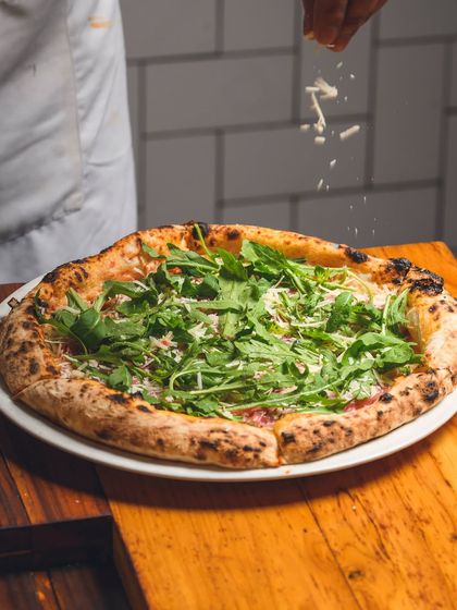 Our Parma Ham & Arugula pizza, getting its final sprinkle of cheese before being boxed up for delivery.