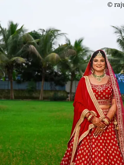 A stunning wide-angle shot of the bride in an open green field. The contrast between her vibrant red lehenga and the lush landscape creates a breathtaking and memorable wedding portrait.