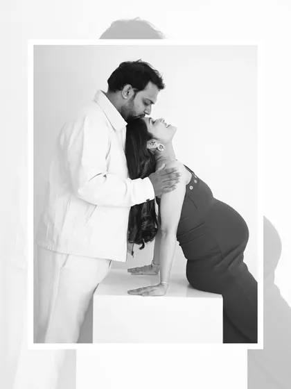 An artistic black and white maternity portrait. The mom-to-be leans forward while her partner kisses her forehead, creating a powerful and emotional silhouette.
