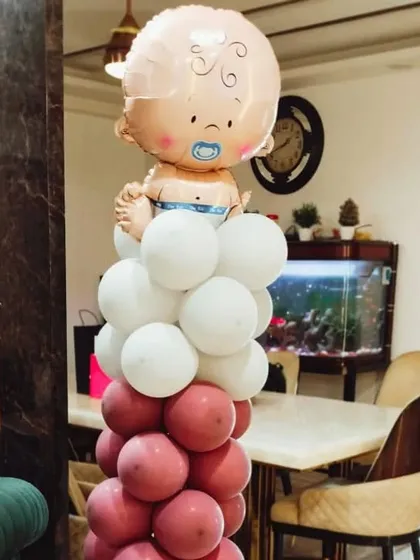 A cute balloon pillar topped with a baby boy foil balloon, perfect for a welcome home decoration or a baby shower. The pink and white color scheme can be customized.