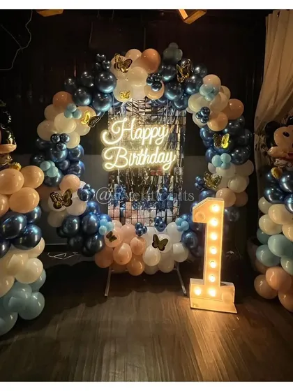A Mickey Mouse themed birthday with a stylish twist. This circular balloon arch uses a cool palette of blue, white, and nude tones, with a 'Happy Birthday' neon sign and Mickey Mouse foil balloons.