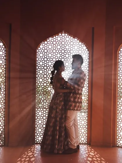 A silhouette of a couple against an intricately carved 'jali' screen, with sunbeams filtering through. This is an example of how I play with light and shadow to create dramatic, artistic, and memorable pre-wedding portraits.