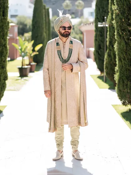 A full-length portrait of the groom in his sage green Tarun Tahiliani sherwani. The emerald neckpiece adds a perfect pop of color, breaking the monotony of the pastel look.