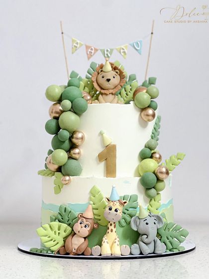 A non-fondant jungle safari theme cake for a first birthday. This two-tiered whipped cream cake is decorated with adorable, handmade fondant animals like a lion, giraffe, and elephant.