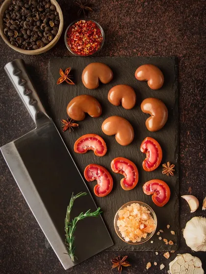 A dark and moody shot of sliced kidneys on a slate board, styled with a large cleaver and spices. This composition is dramatic and masculine, positioning the product as a premium choice for serious cooks.