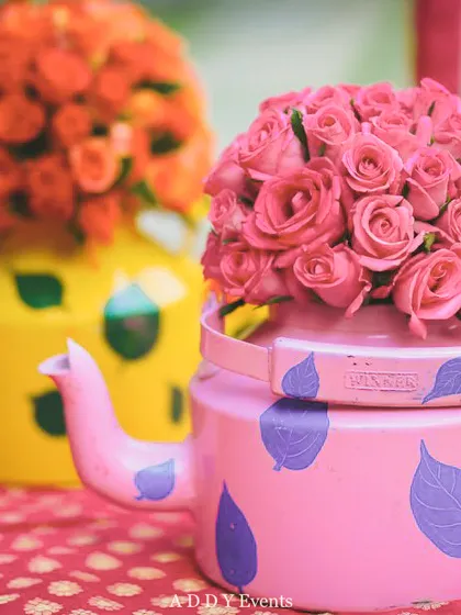 Quirky and colorful hand-painted kettles used as unique vases for pink and orange roses.