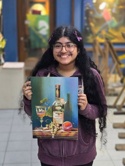 A happy and proud student holds up her completed oil pastel still life, a wonderful achievement that reflects her hard work and artistic growth.