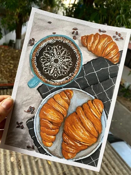 A cozy morning scene featuring coffee and croissants, with a delicate mandala drawn into the latte art. This is an example of my food illustration work, where I use markers and paint to capture delicious details.