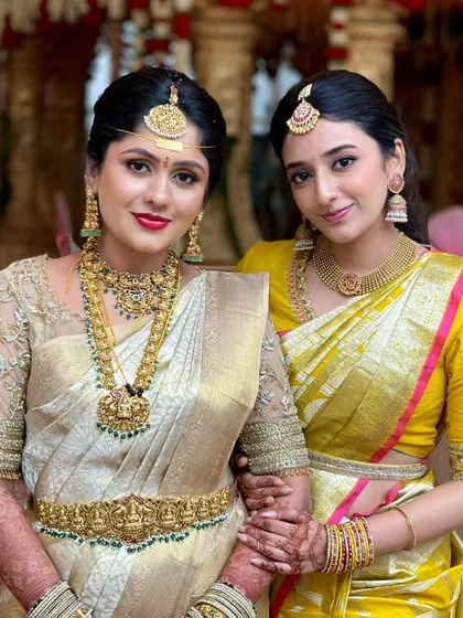 A bride and her bridesmaid. The bridesmaid wears a bright yellow Kanchipuram saree with a custom blouse featuring simple embroidery on the sleeves.