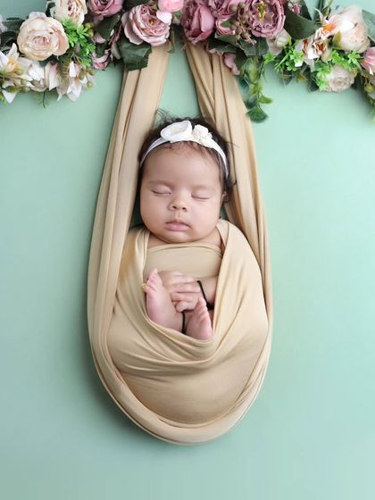 A slightly different angle of the hanging floral sling, showcasing the baby's peaceful sleep and the beautiful arrangement of flowers above.