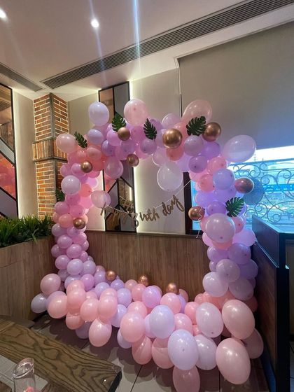 A beautiful pastel pink and purple balloon arch in a restaurant. The addition of faux leaves and chrome gold balloons gives it a modern and chic look.