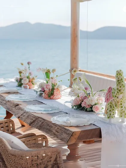 An intimate table setting for a seaside lunch in Turkey. The rustic wooden table and delicate florals perfectly complement the natural beauty of the coastline, creating a serene dining experience.