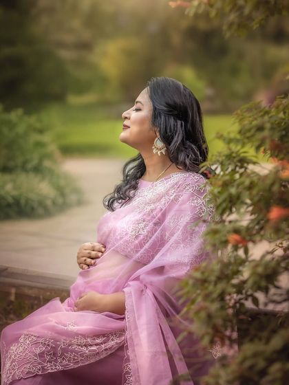 A serene solo portrait of a mother-to-be, basking in the soft, misty air. Her delicate pink saree and the natural garden setting create a peaceful and ethereal image, capturing a moment of pure calm.