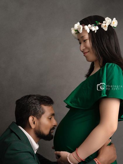 A sweet and simple couple's pose against a solid grey background. The partner's gentle kiss on the baby bump is a timeless expression of love.