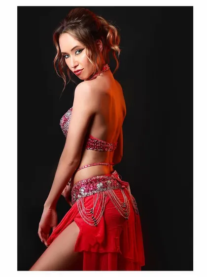 A portrait of a belly dancer in a stunning red and silver costume, captured against a black background to highlight the outfit's details.