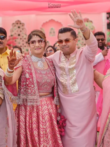 The happy couple at their pink Haldi, waving to their guests. Their coordinated pink outfits perfectly match the vibrant theme of the event.