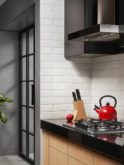 A pop of red from a kettle adds life to this minimalist kitchen. I designed the space with a white brick backsplash, black granite countertops, and handle-less wood cabinets for a clean, functional, and timeless look.